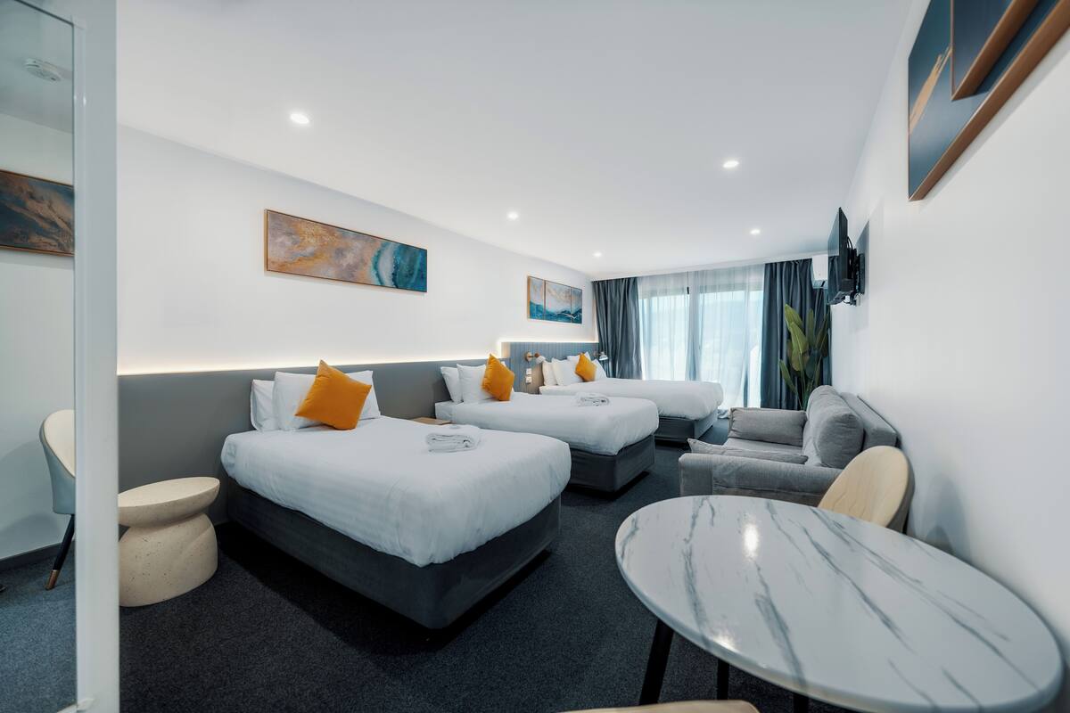 A hotel room with two beds, a sofa, a round table, and a TV mounted on the wall.