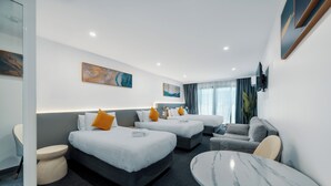 A hotel room with two beds, a sofa, a round table, and a TV mounted on the wall.
