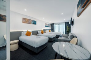 A hotel room with two beds, a sofa, a round table, and a TV mounted on the wall.