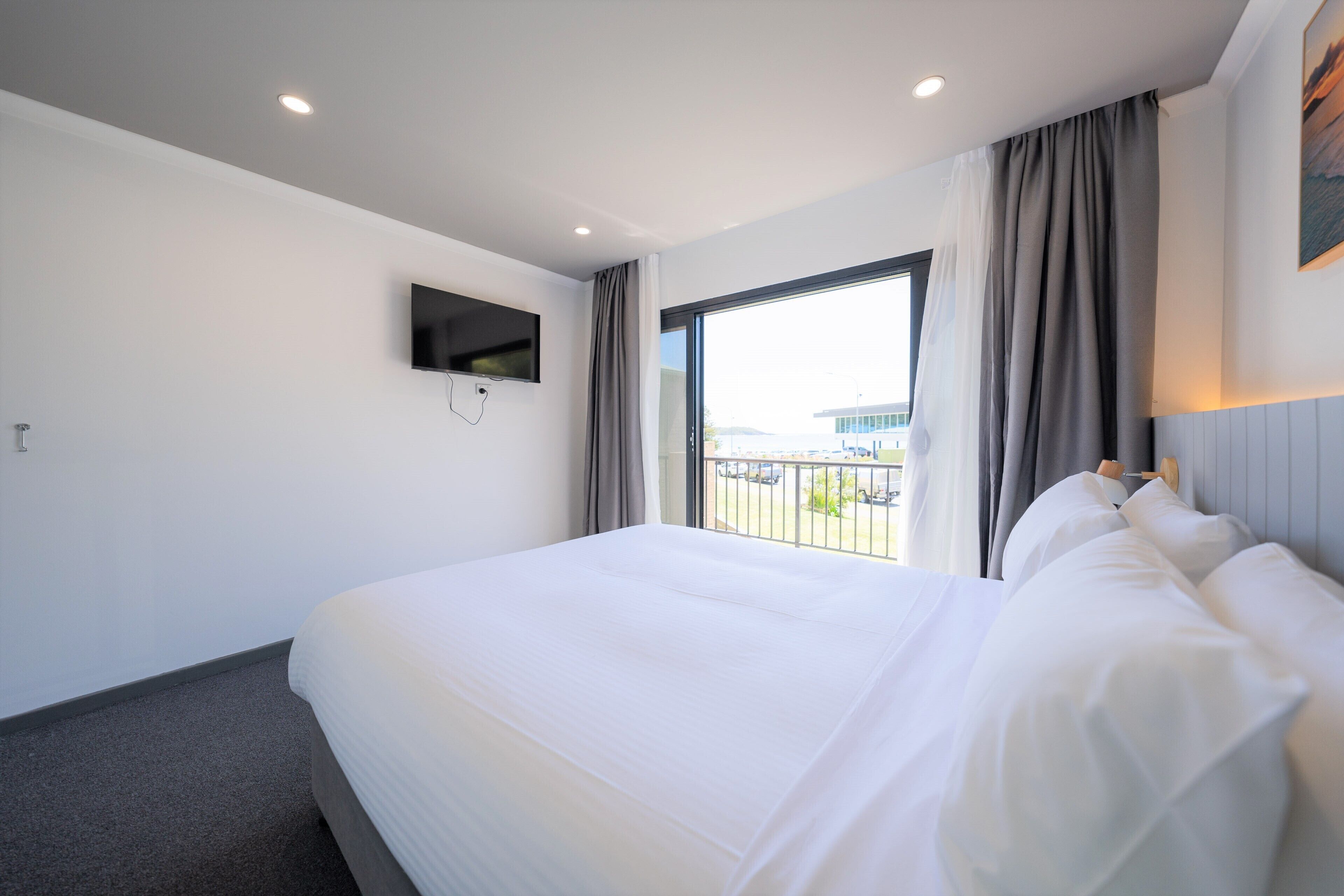 Habitación de hotel con una cama grande, un televisor de pantalla plana montado en la pared y una ventana con cortinas.
