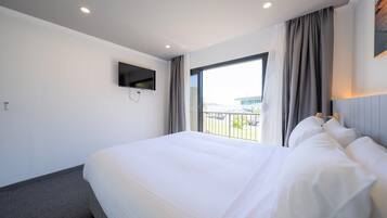 Habitación de hotel con una cama grande, un televisor de pantalla plana montado en la pared y una ventana con cortinas.