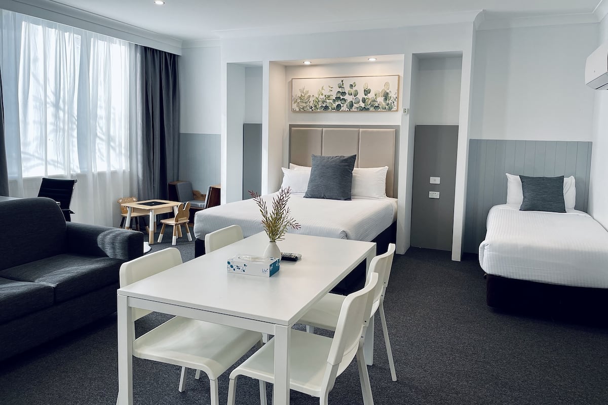 Una habitación de hotel moderna con cama, sofá, mesa de comedor y un escritorio pequeño.