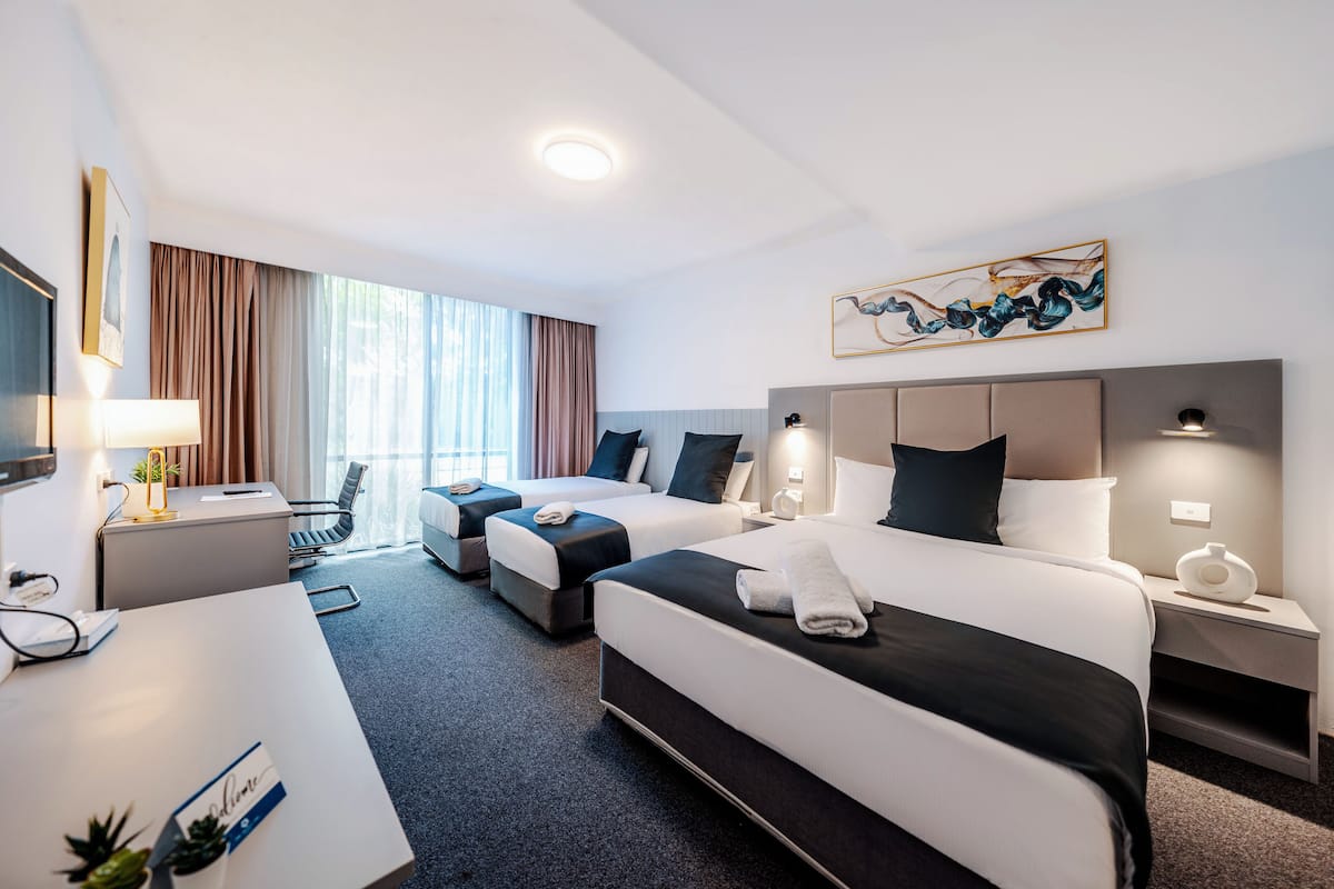 Una habitación de hotel con dos camas, un escritorio, una silla, un televisor y un ventanal con cortinas.