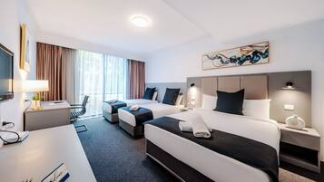 A hotel room with two beds, a desk, a chair, a TV, and a large window with curtains.