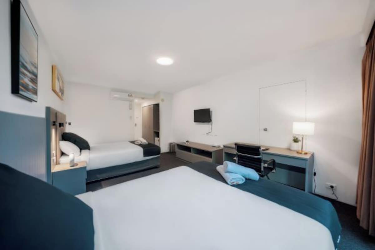 A hotel room with two beds, a desk, a chair, a TV, and a mirror.