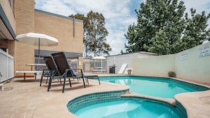 A swimming pool with a tiled edge, surrounded by a brick building and a white fence.