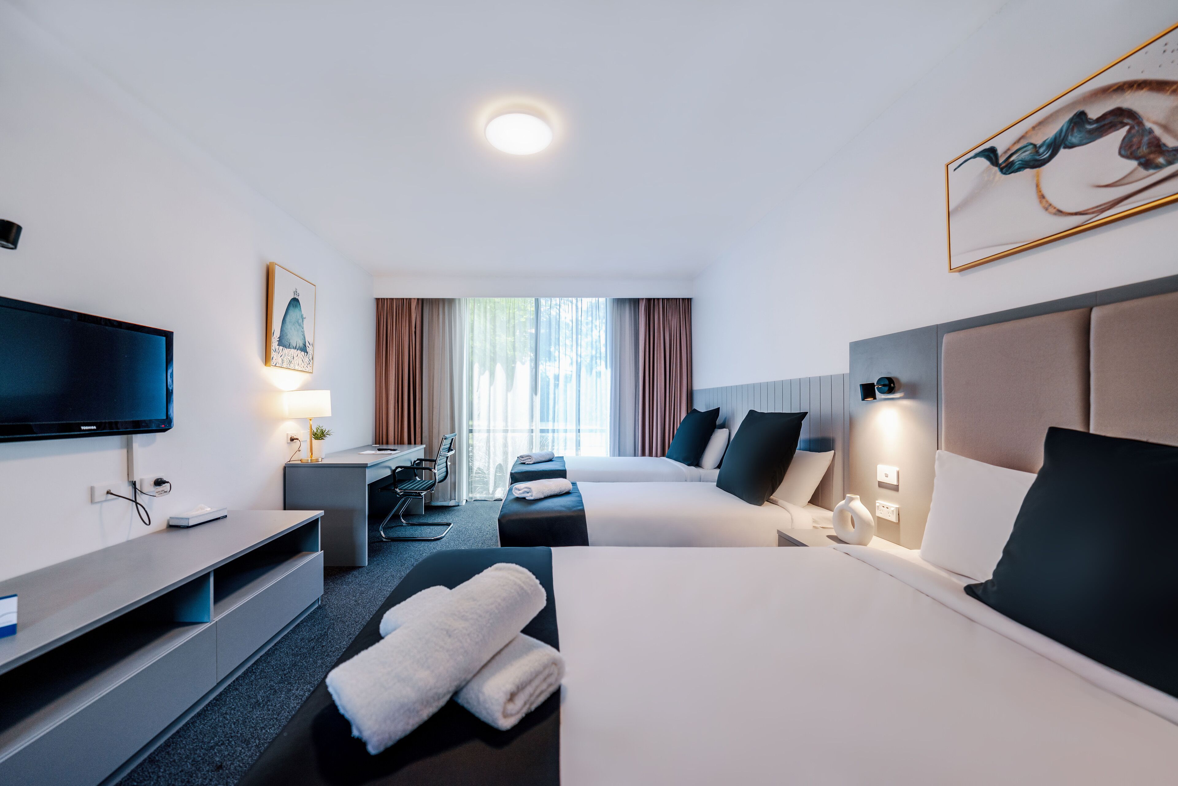 Una habitación de hotel con dos camas, televisión, escritorio y ventana con cortinas.