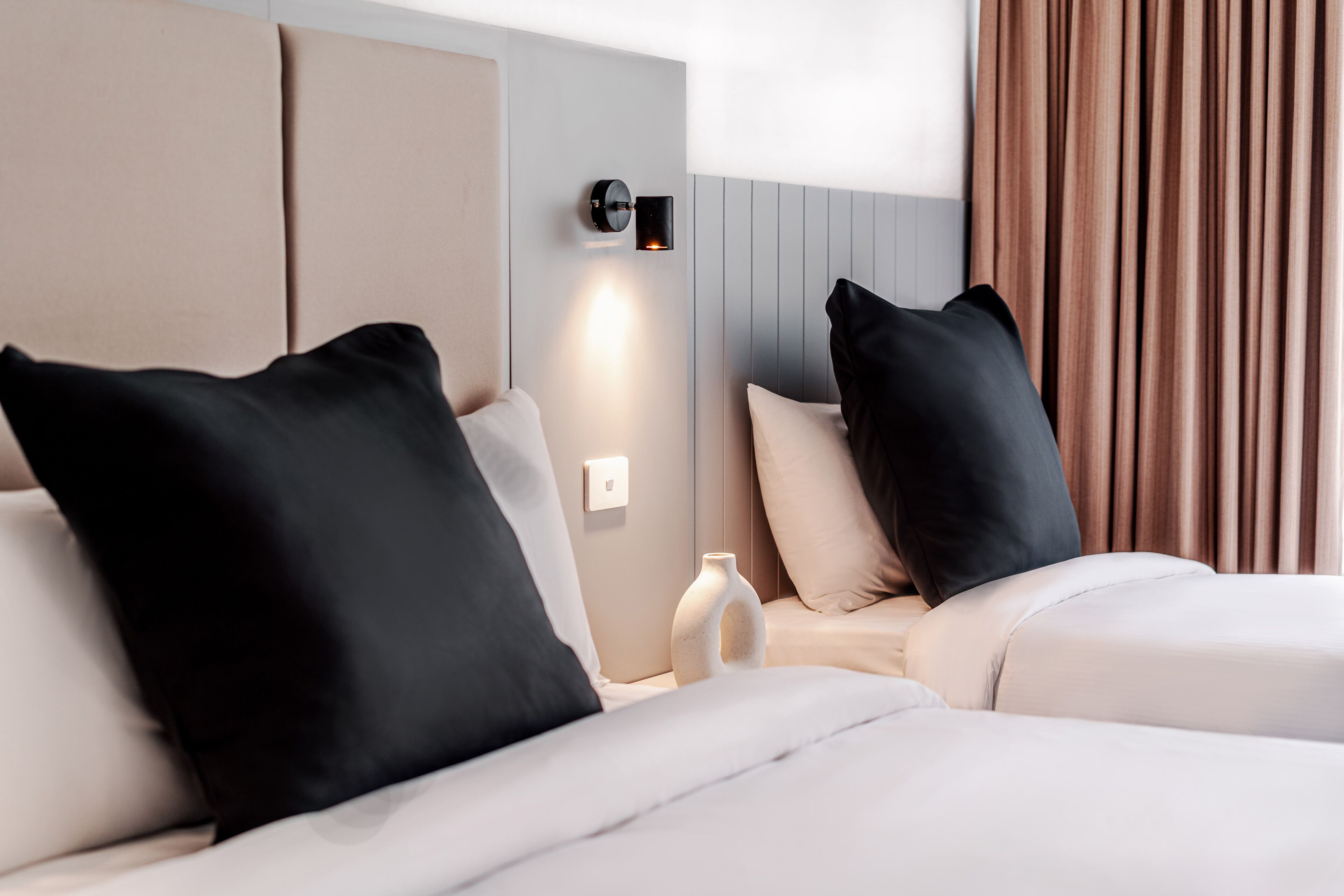Camera d'albergo con due letti, un comodino, un vaso e una lampada a parete.