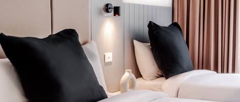 Camera d'albergo con due letti, un comodino, un vaso e una lampada a parete.