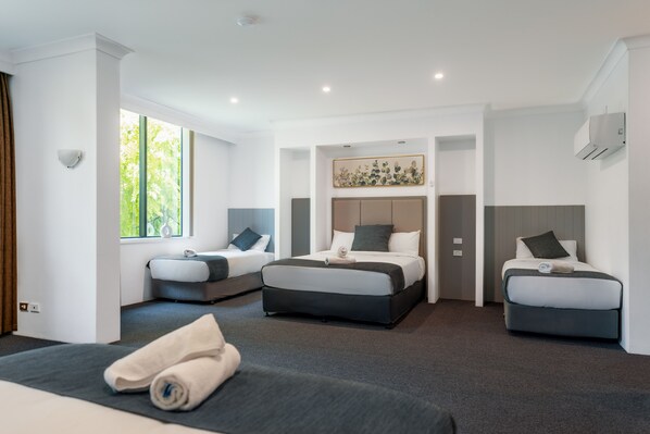 Una habitación de hotel moderna con tres camas, un ventanal grande y un equipo de aire acondicionado instalado en el techo.