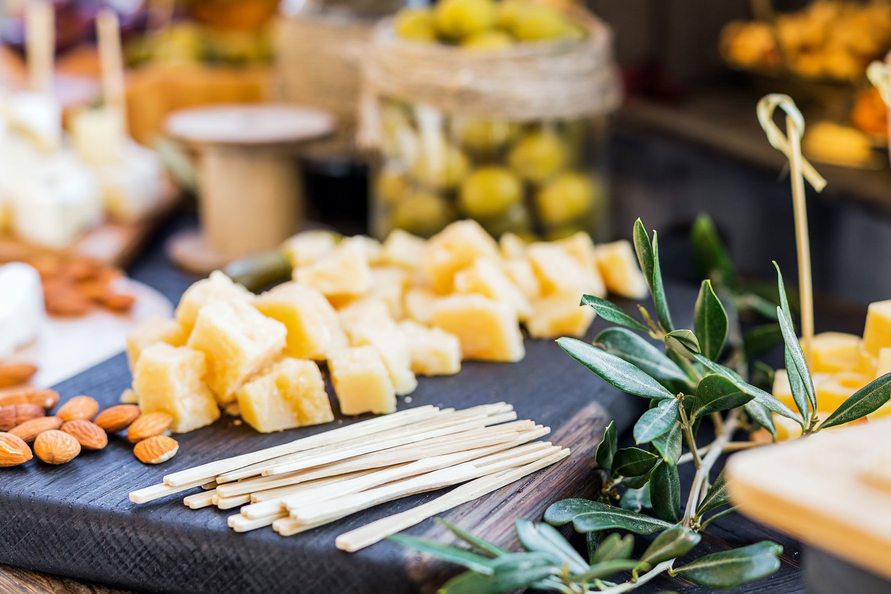 A variety of cheeses and nuts on a slate board, with olive branches and toothpicks.