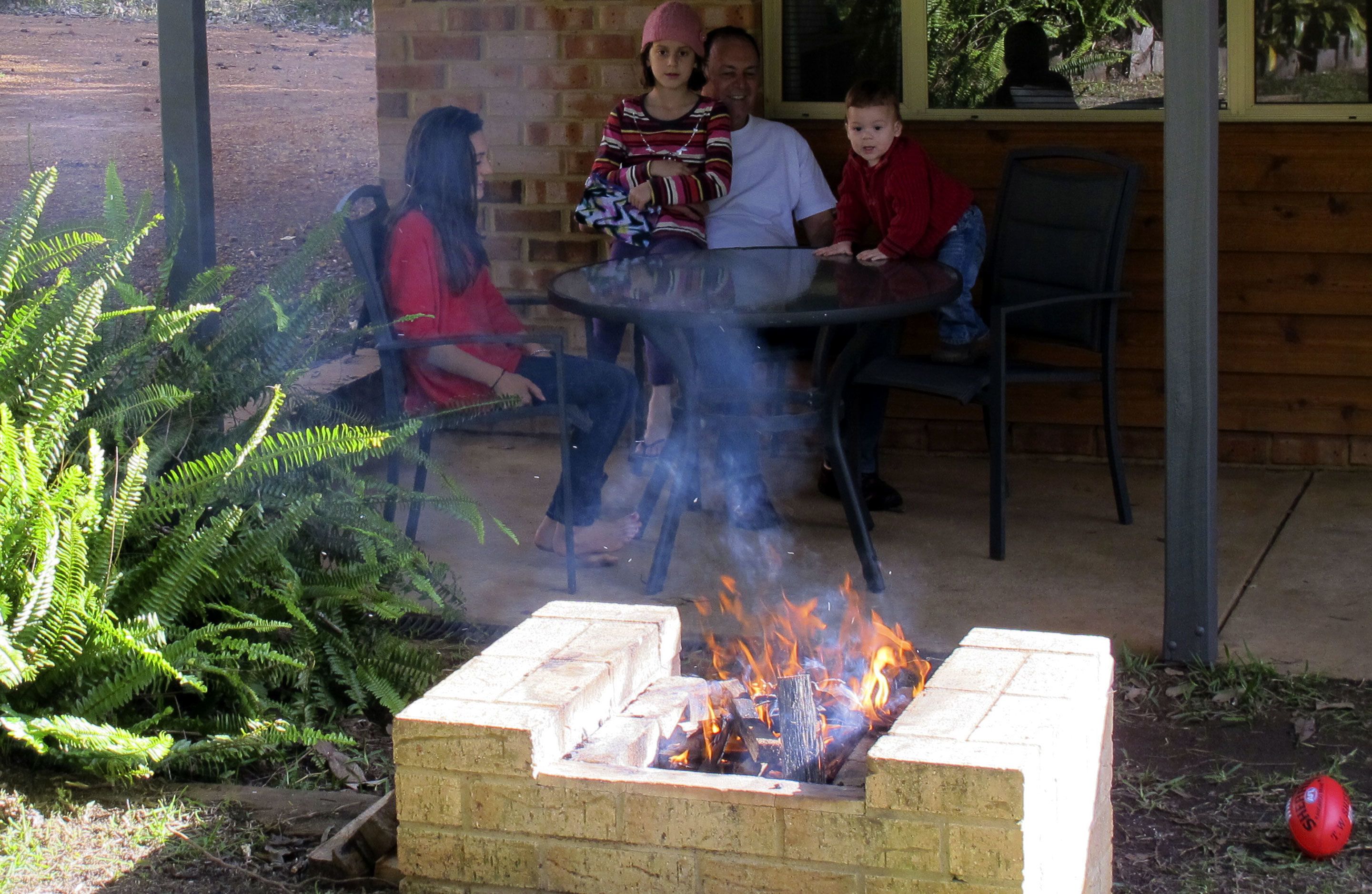 A fire pit with people around it, a brick wall, and outdoor seating.