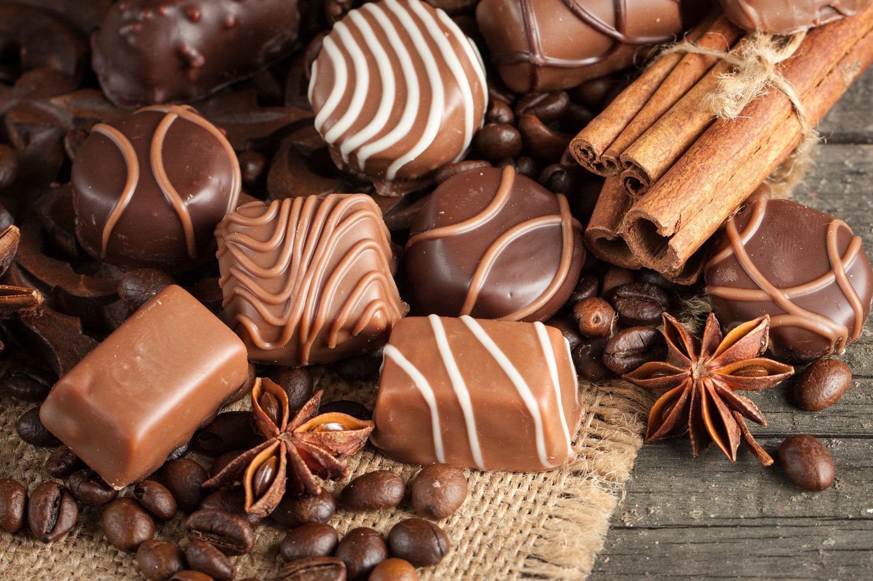 Un assortiment de chocolats et d’épices, notamment de l’anis étoilé et des bâtons de cannelle, disposés sur une surface rustique.