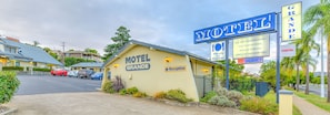 Ein Motel namens 'GRANDE' mit Empfangsschild, Parkplatz und Hinweisschild, das Annehmlichkeiten wie Verpflegung, Klimaanlage, Salzwasserpool, Stellplätze für Wohnwagen und WLAN auflistet.
