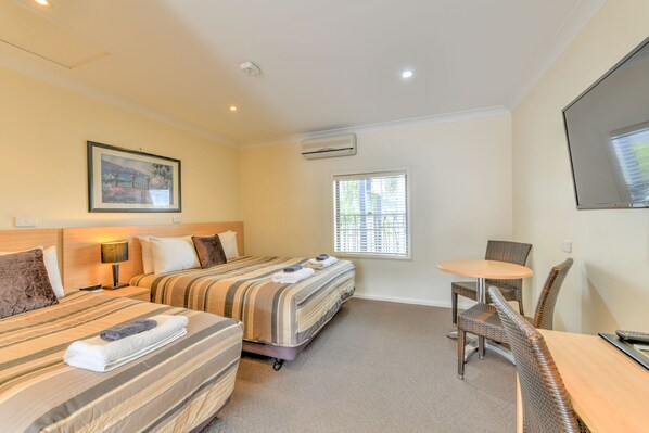 Habitación de hotel con dos camas, una pequeña mesa de comedor y un televisor.