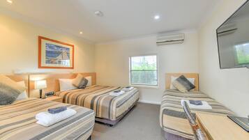 Una habitación de hotel con dos camas, televisión, aire acondicionado, ventana y un cuadro en la pared.