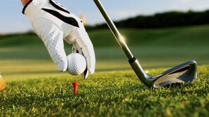 Primer plano de la cabeza de un palo de golf y una pelota sobre un tee en un campo de césped.