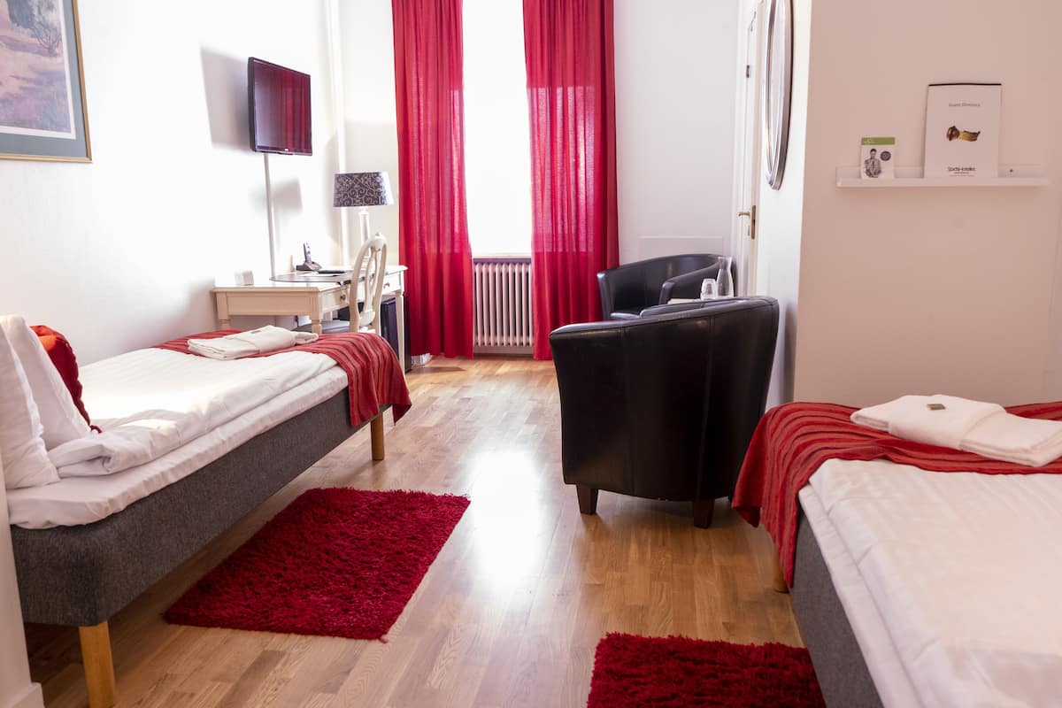 Ein Hotelzimmer mit zwei Betten, einem Schreibtisch, einem Sessel, einem Fernseher und einem roten Vorhang.