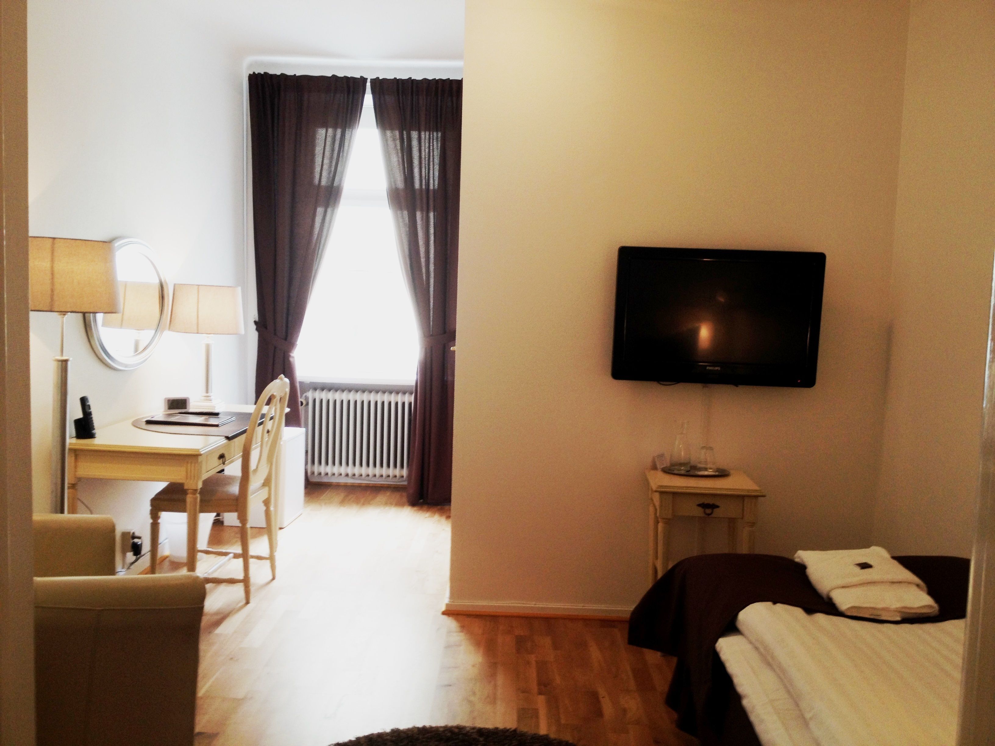 Een hotelkamer met een bed, een televisie, een bureau met stoel, een lamp en een raam met gordijnen.