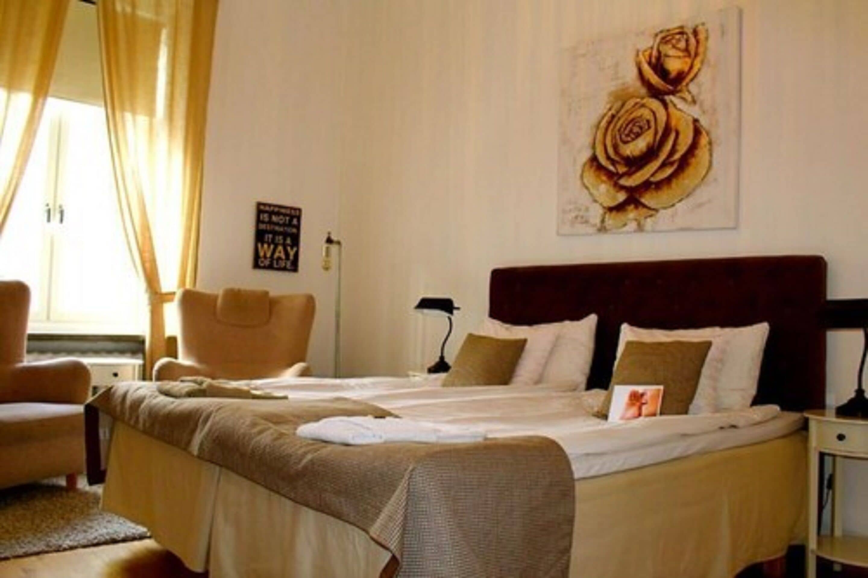 A hotel room with a large bed, two bedside tables, a chair, and a painting of roses on the wall.