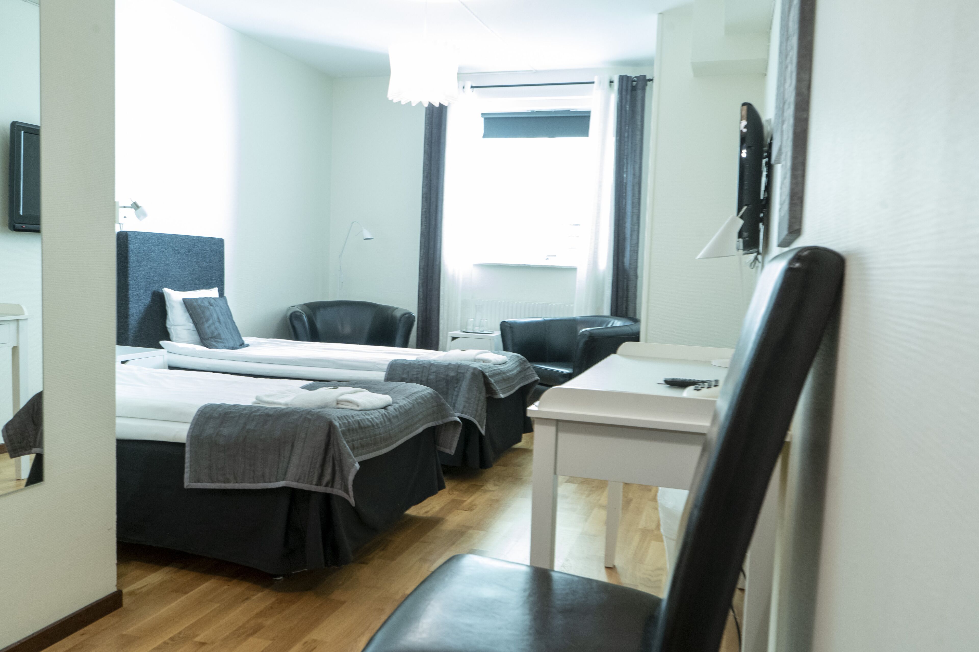 A hotel room with two beds, a desk, a chair, and a window with curtains.
