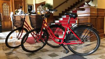 A red bicycle with a basket and a black basket, parked indoors with a checkered floor and a staircase in the background.