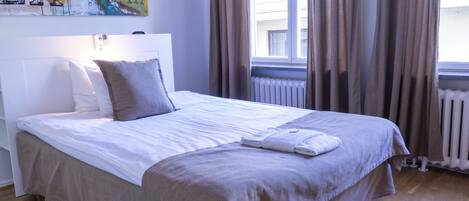 A neatly made bed with a white and beige bedspread, a folded towel, and two pillows. A large abstract painting is on the wall above the bed.