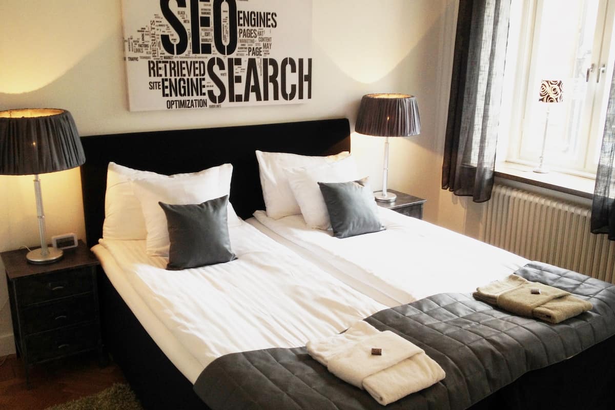 Ein Hotelzimmer mit einem großen Bett, zwei Nachttischen, einer Wandcollage aus Wörtern und einem Vorhangfenster.