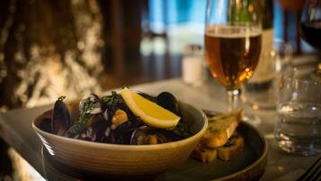 En skål med muslinger, citron og persille, et glas øl og en flaske vin på et bord.