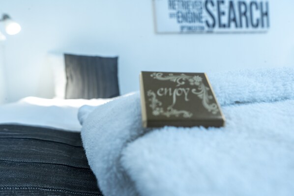 A neatly made bed with a white blanket and a pillow, a small decorative item on the pillow, and a wall with a sign that reads "RENEWED ENGINE SEARCH". - Stadshotellet Kristianstad (Kristianstad)