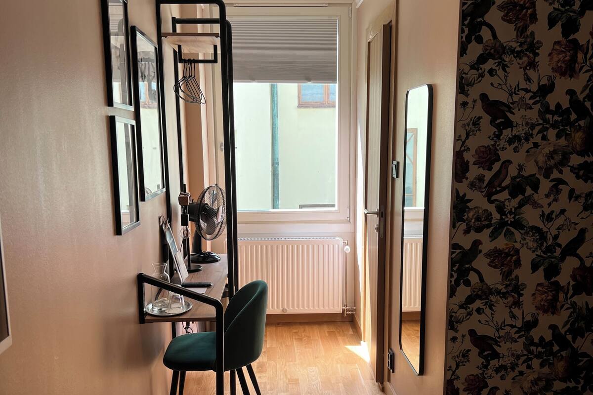 Ein Hotelzimmer mit Bett, Schreibtisch mit Stuhl, Heizkörper und einem Fenster mit Jalousien.