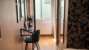 Une chambre d’hôtel avec un lit, un bureau et une chaise, un radiateur et une fenêtre avec des stores.