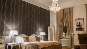 Quarto com cama, duas mesas de cabeceira, um lustre, janela com cortinas e um radiador.