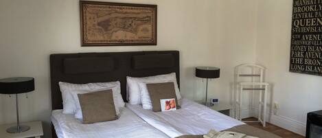 A neatly made bed with white linens and brown pillows, a framed map on the wall, and a sign listing nearby locations.
