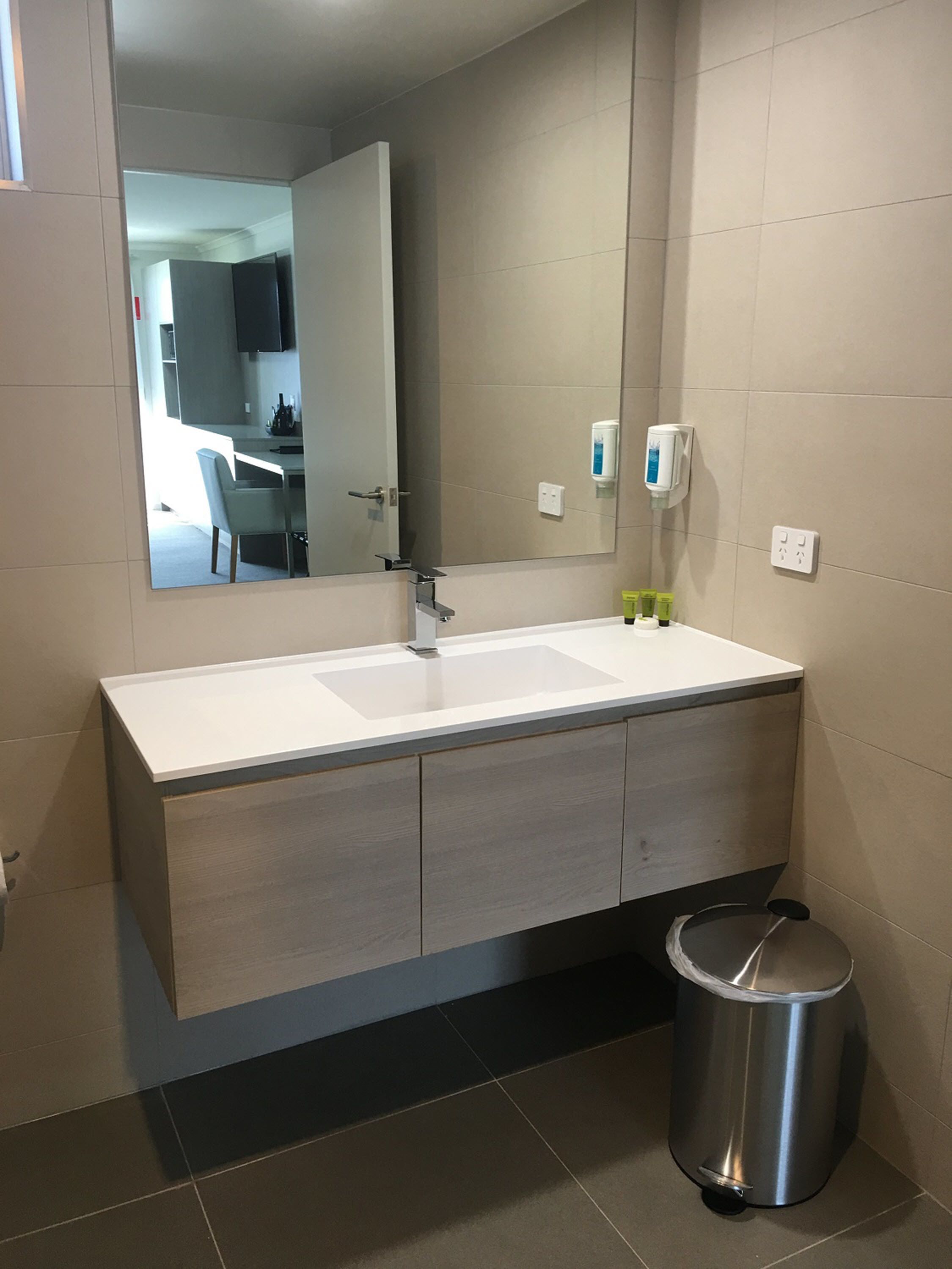 Une salle de bain moderne avec un grand miroir, un lavabo et une poubelle.