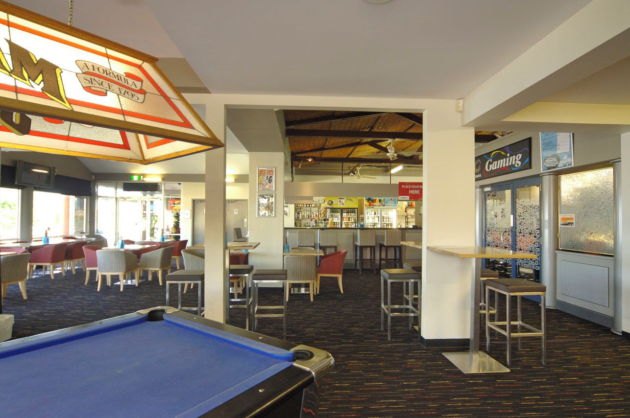 Una mesa de billar en una sala con varias mesas y sillas, un área de bar y una zona de juegos.
