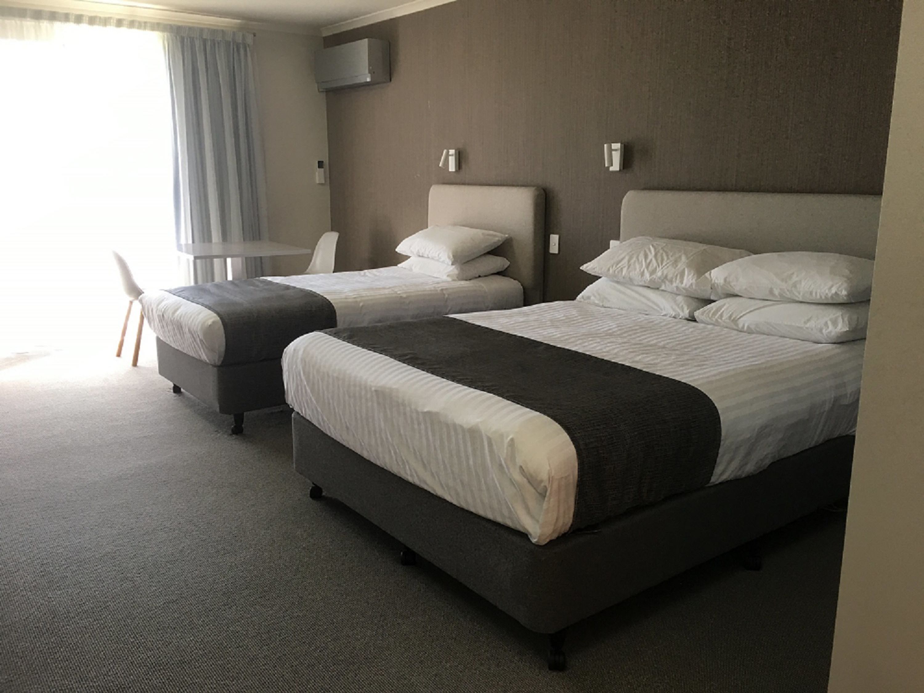 A hotel room with two beds, a desk, and a chair.
