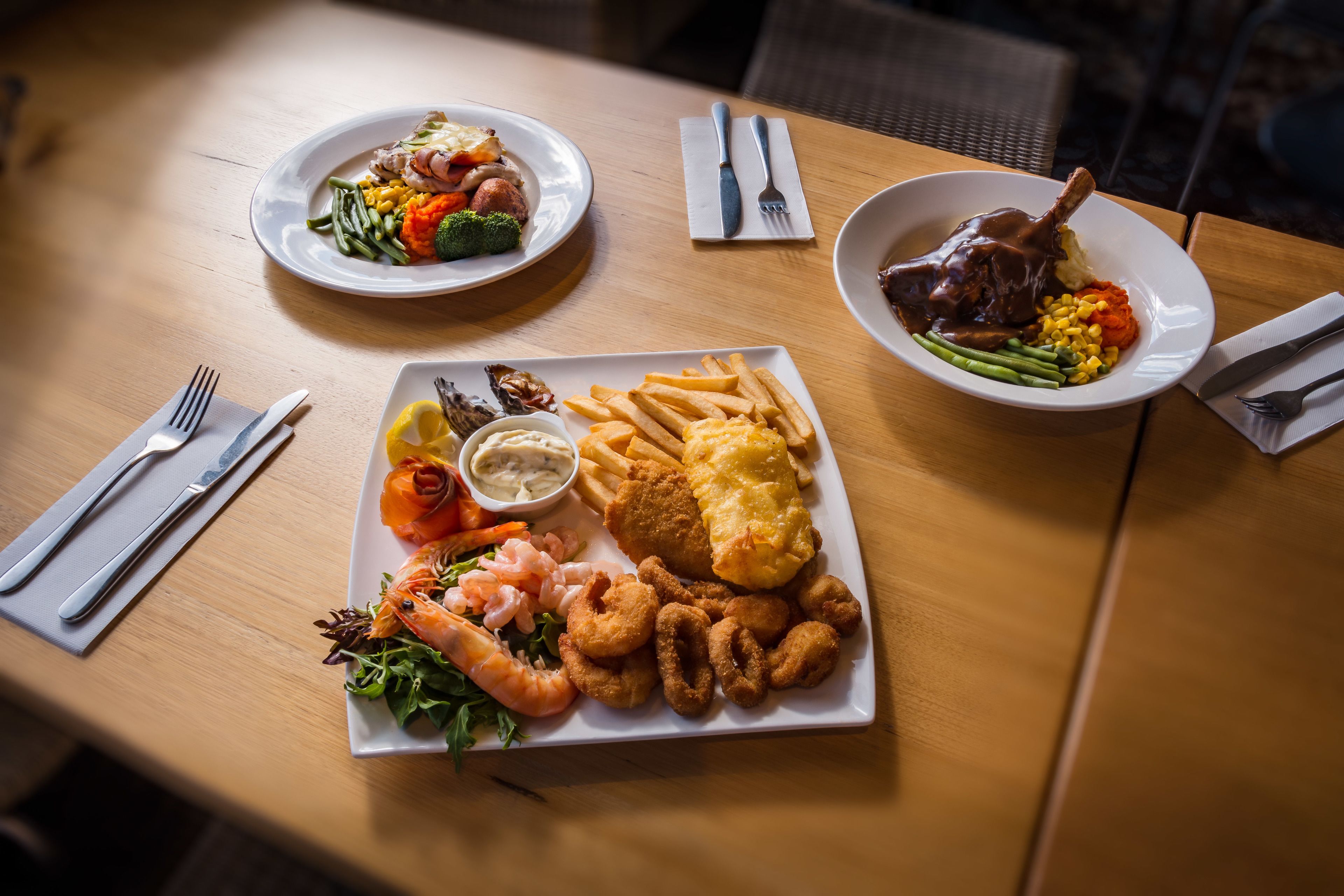 A table with three plates of food, including seafood and vegetables.