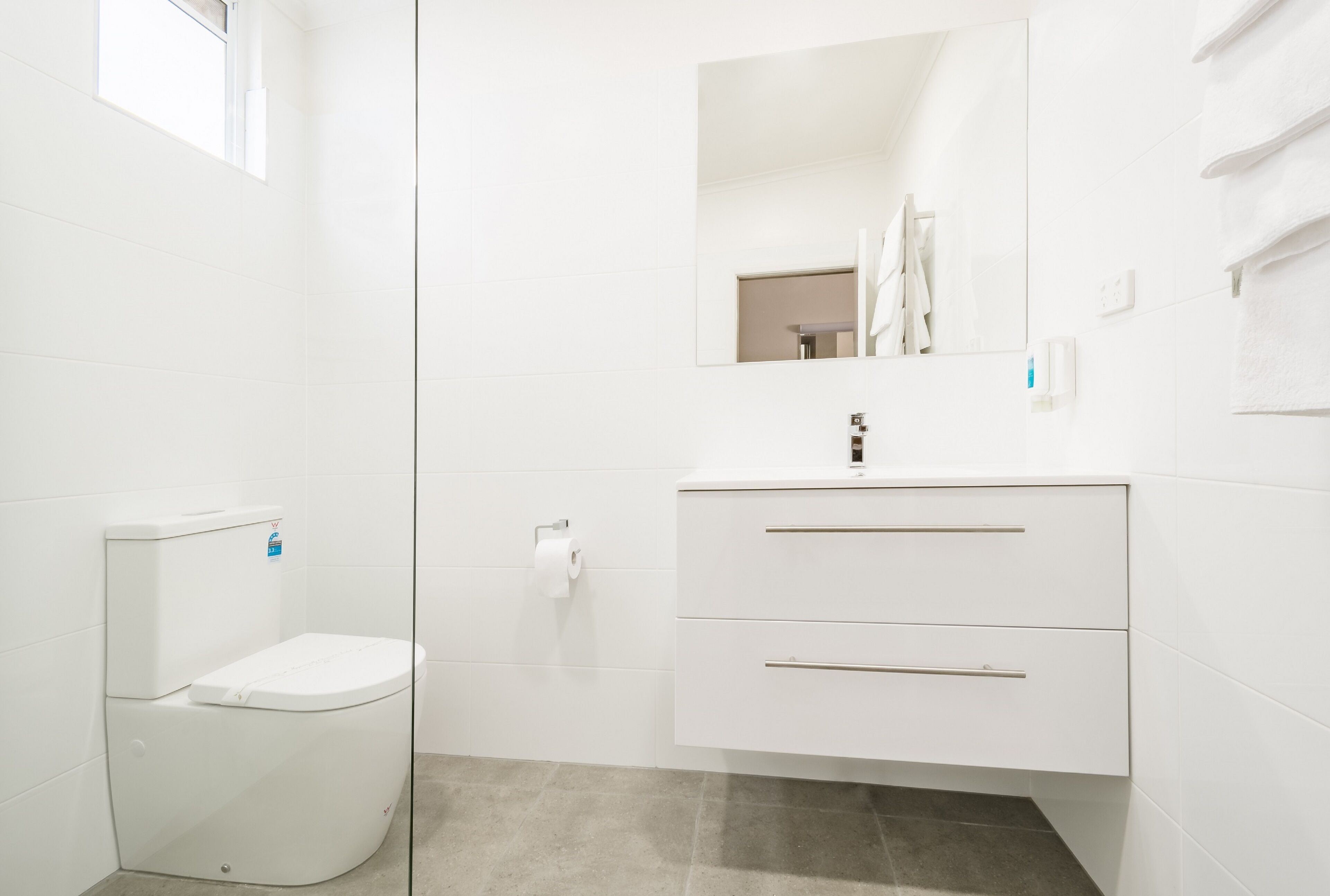 Un baño moderno con inodoro, lavamanos con espejo y un perchero para toallas.