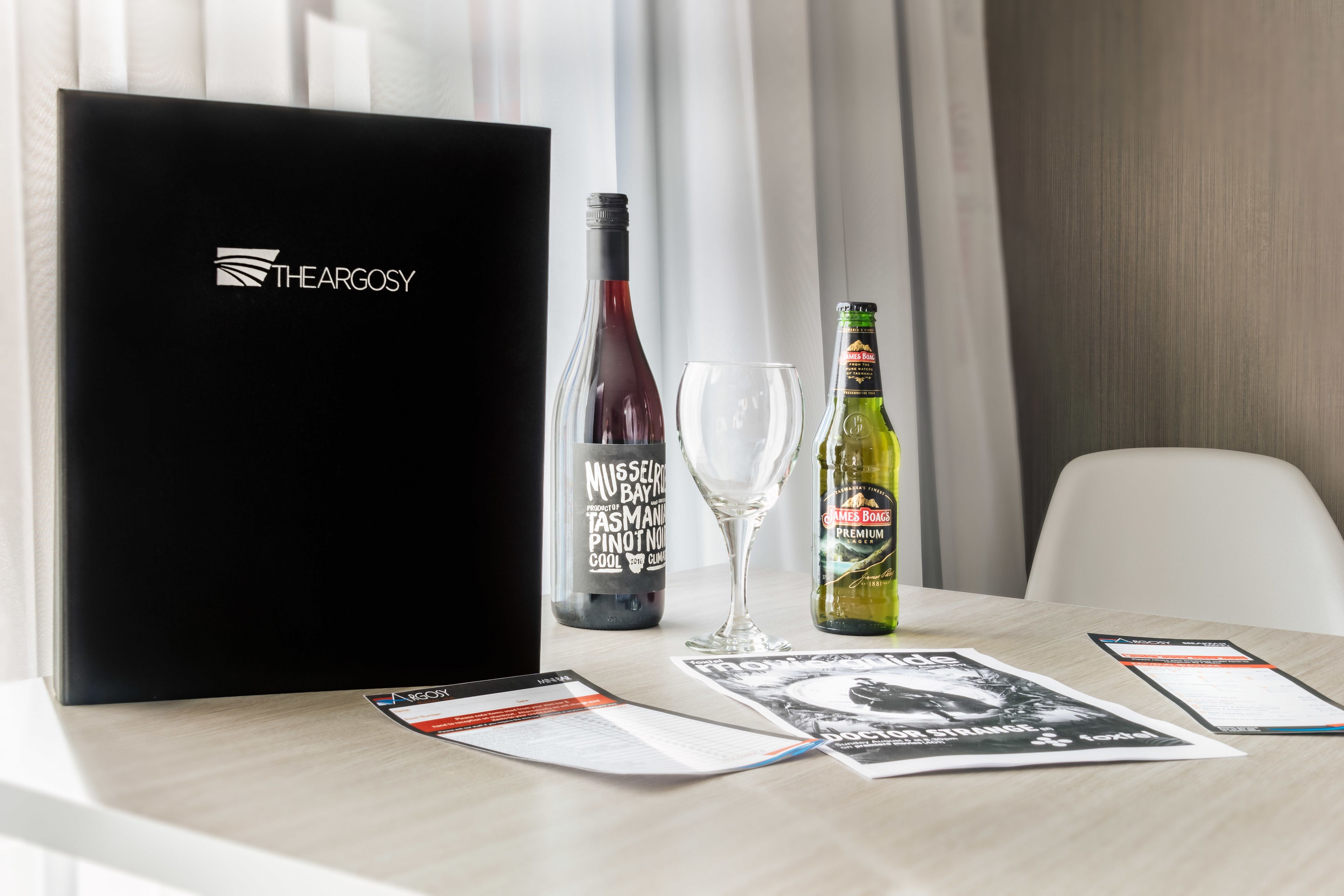 A laptop with a logo, a wine bottle, a wine glass, and a bottle of James Bond premium wine on a table with menus.