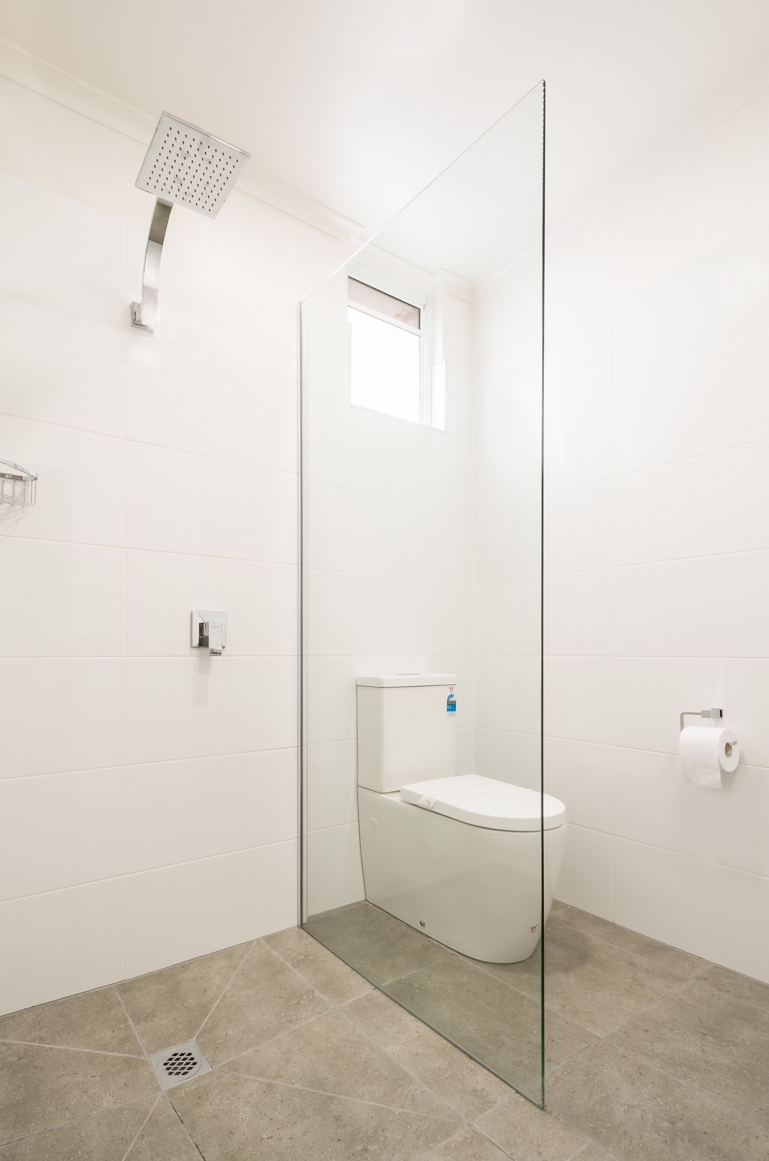 A modern bathroom with a glass-enclosed shower, a toilet, and a small window.