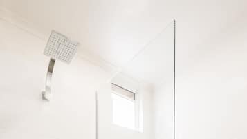 A modern bathroom with a glass-enclosed shower, a toilet, and a small window.