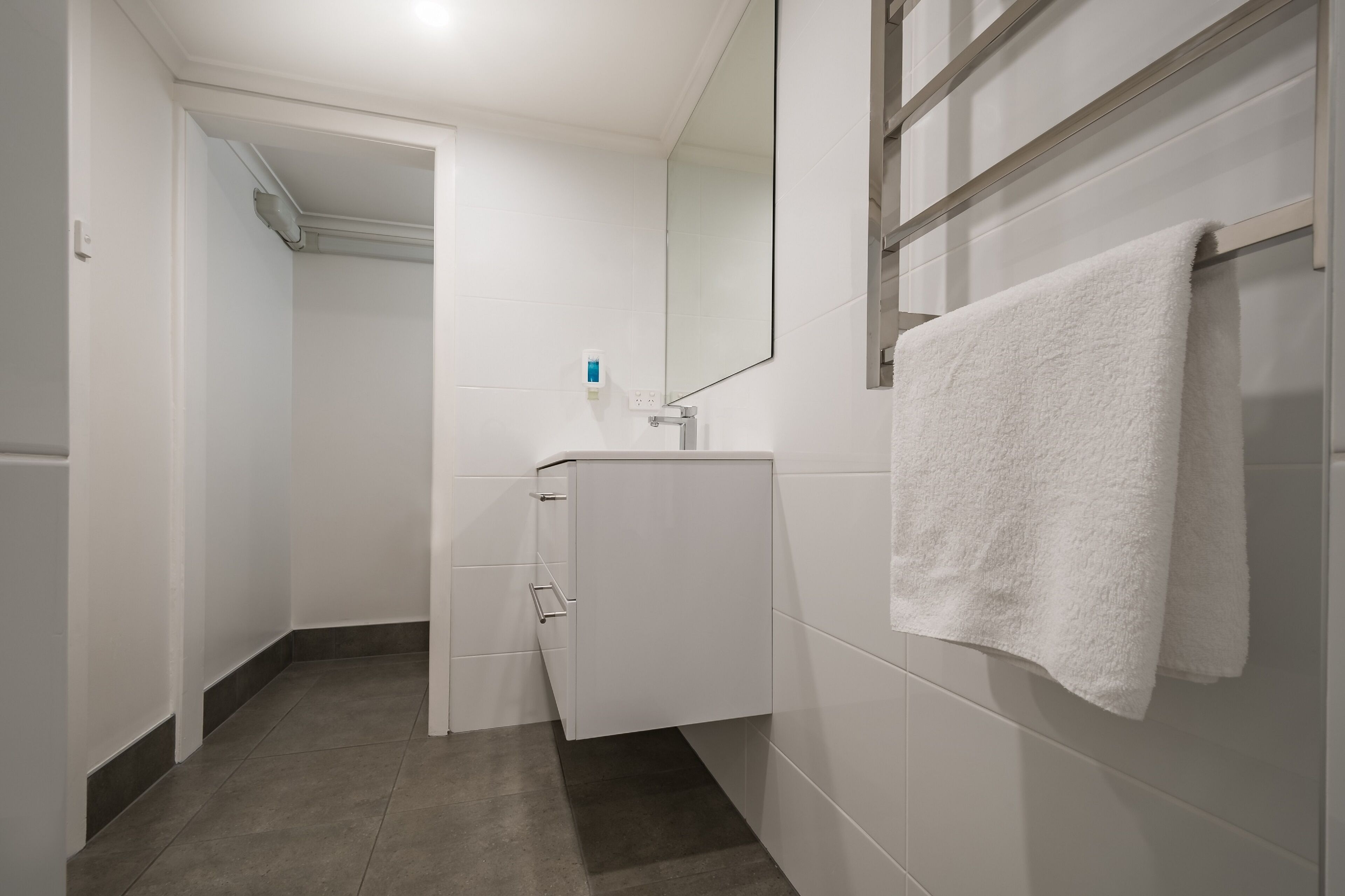 A modern bathroom with a white sink, a towel hanging on the wall, and a mirror above the sink.