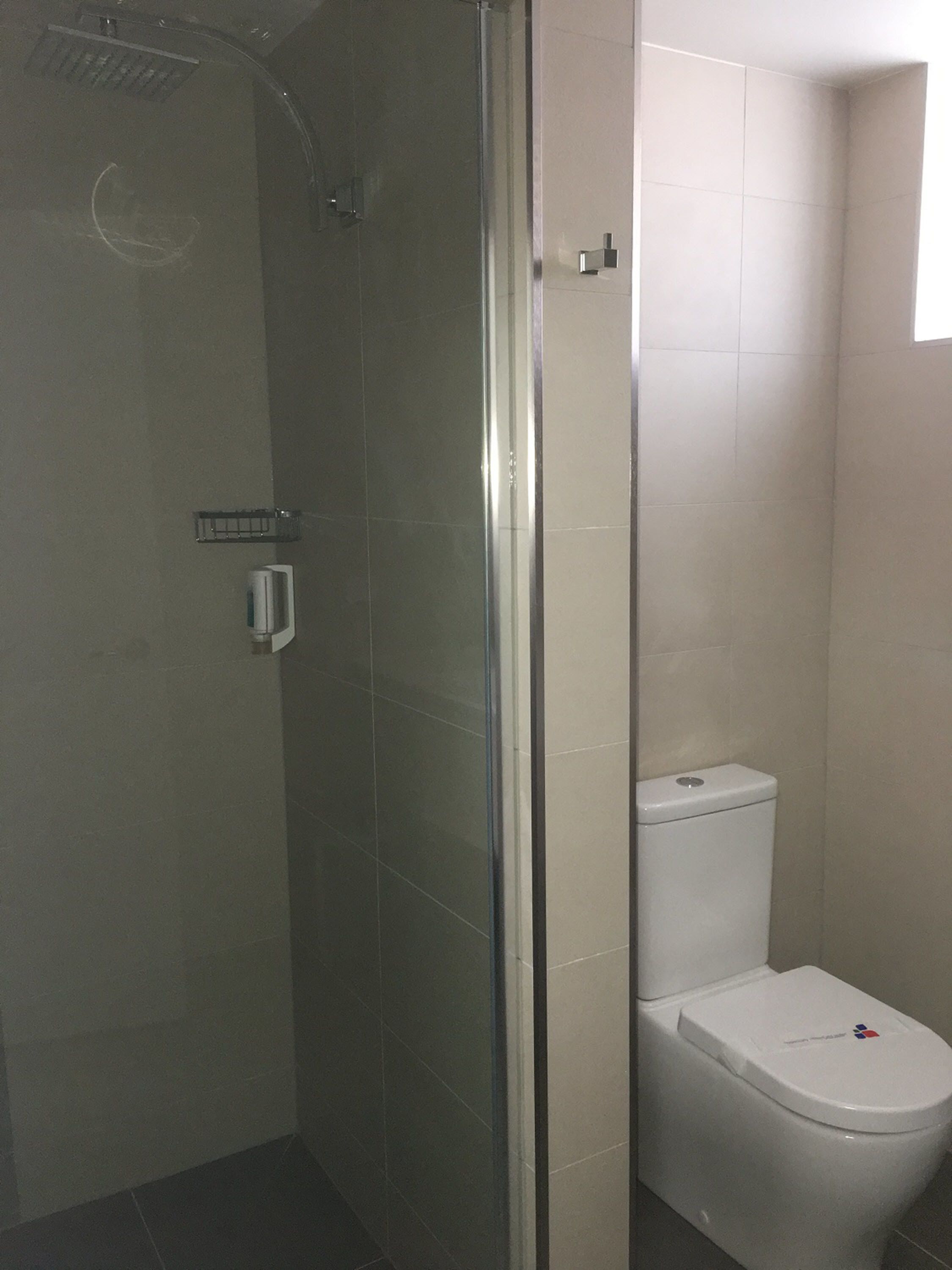 A bathroom with a glass-enclosed shower, a white toilet, and a small shelf.