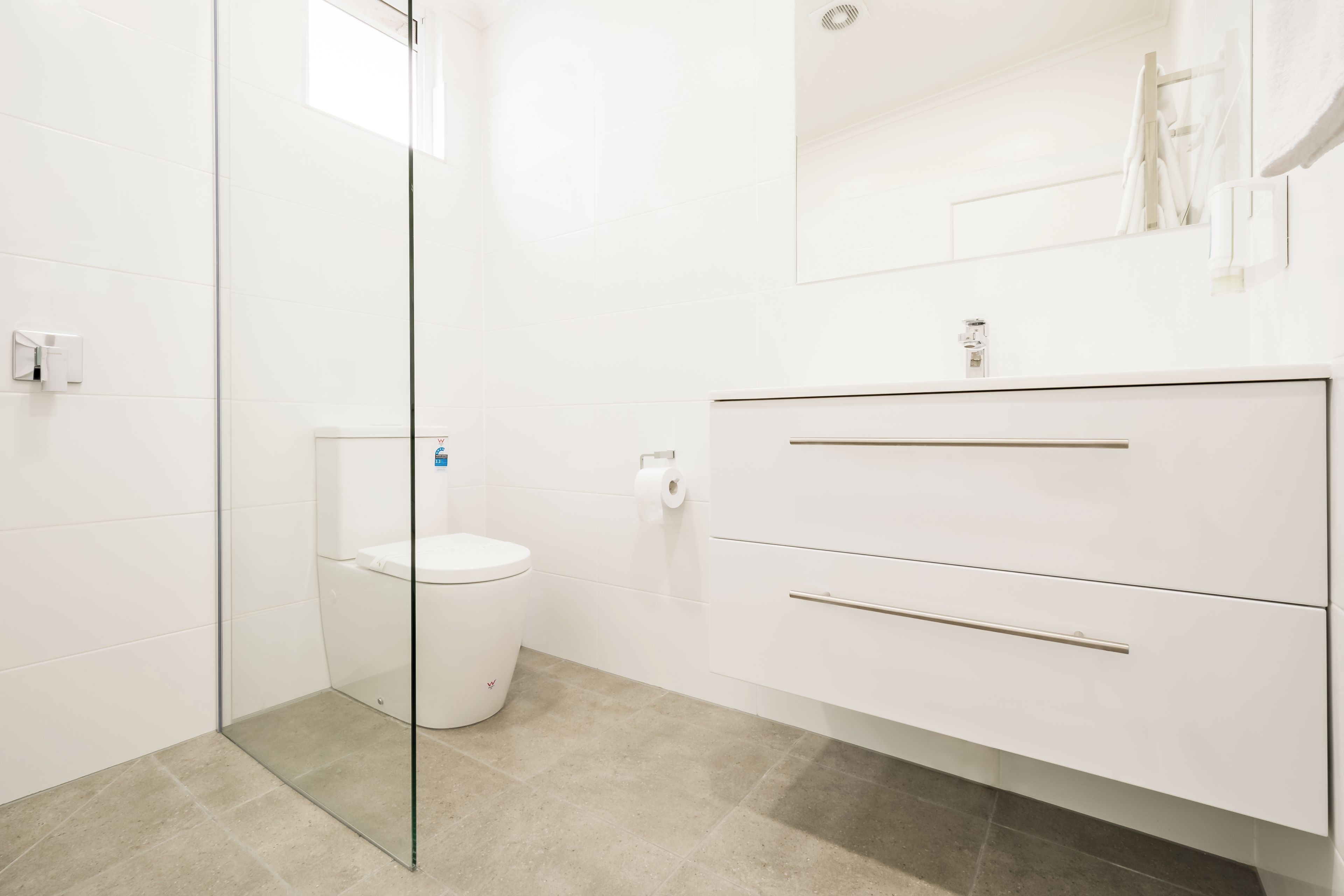 Un bagno moderno con un water, cabina doccia in vetro e un mobile lavabo con specchio.