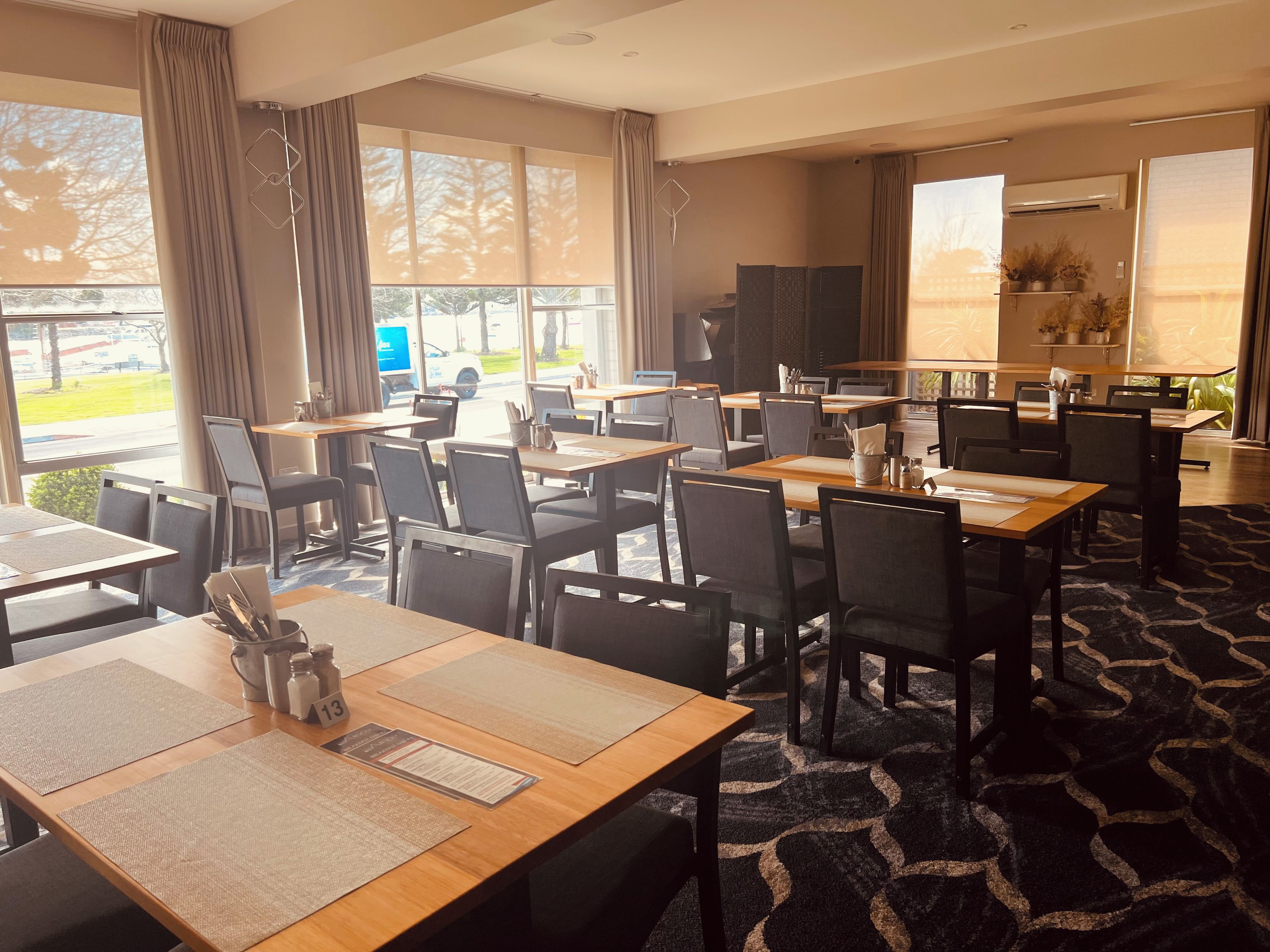 Une salle à manger d’hôtel avec plusieurs tables et chaises, un téléviseur et de grandes fenêtres équipées de rideaux.