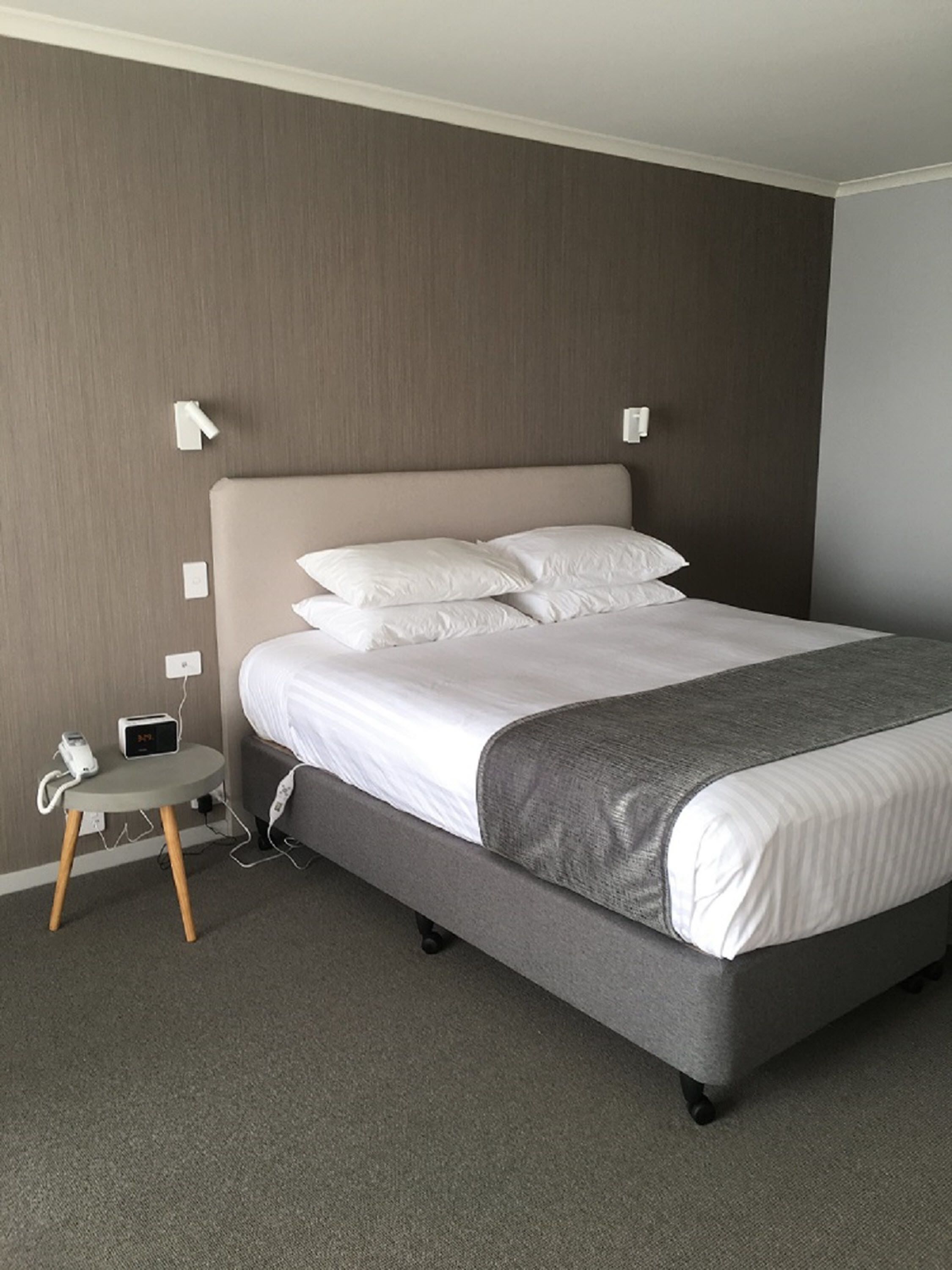 A neatly made bed with white linens and a grey blanket in a hotel room.