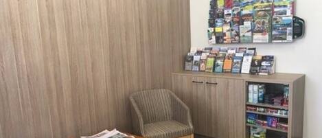 Une pièce avec un mur en bois, une chaise, une table avec des brochures et une bibliothèque remplie de livres et de magazines.