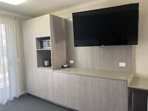 A modern room with a built-in TV, a microwave, and a kettle on a shelf. - The Argosy (East Devonport)