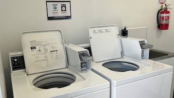 Une laverie publique équipée de deux machines à laver et d’un sèche-linge, d’un extincteur fixé au mur et d’un panneau indiquant l’utilisation d’un extincteur à poudre de type A:B(E).
